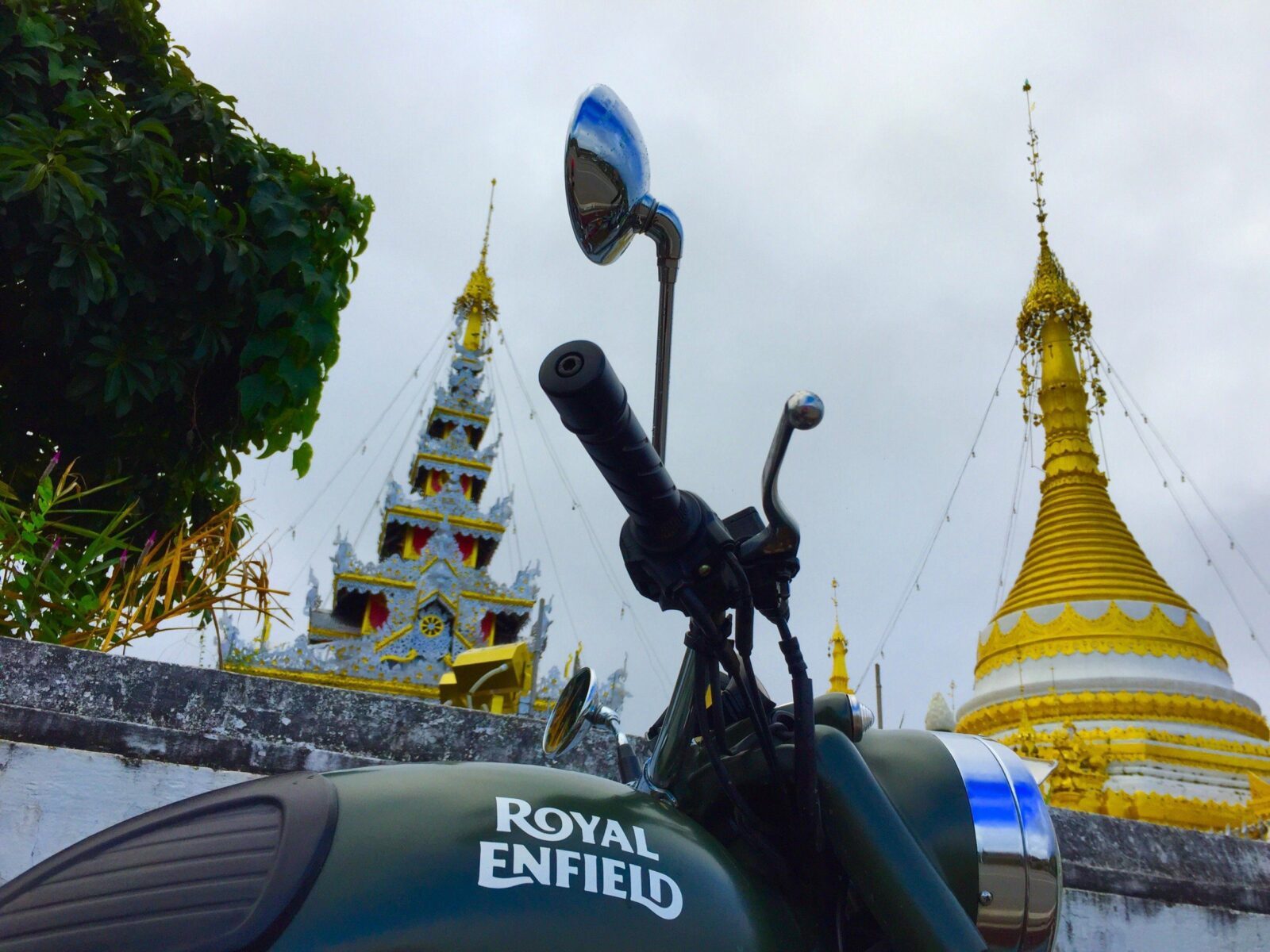 Burmese-style golden chedi seen behind the mirror of a Royal Enfield motorcycle in northern Thailand