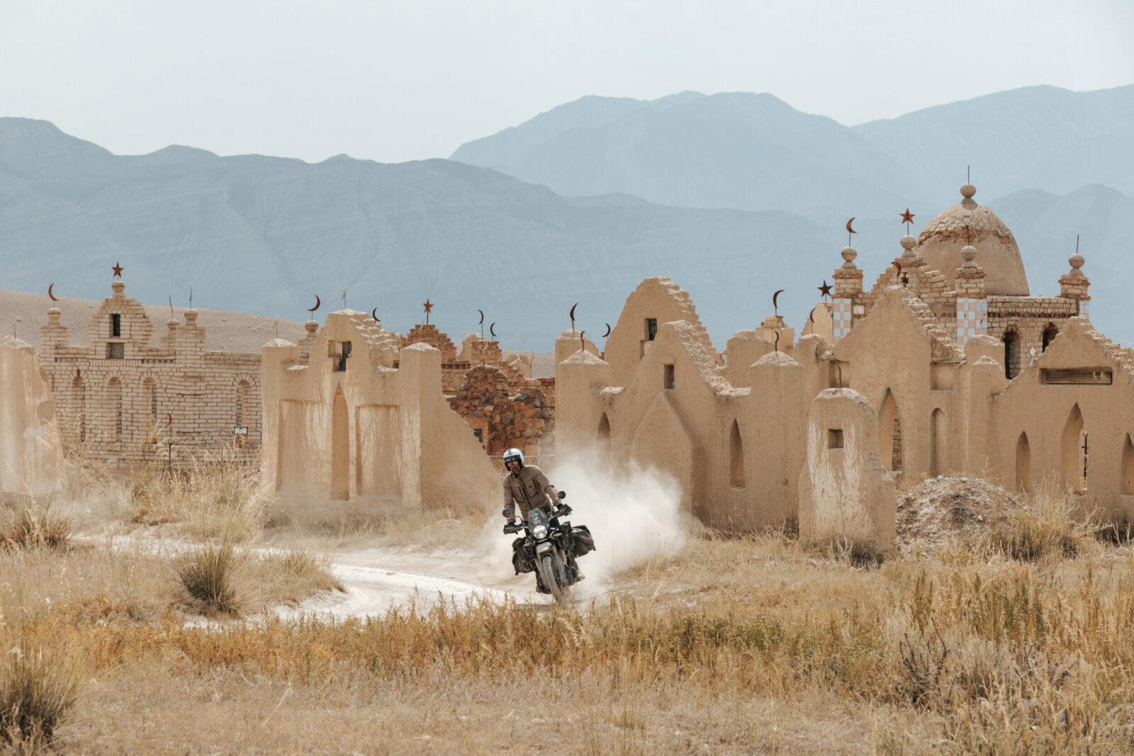 Moto sur une piste devant d'anciens mausolées nomades, près de Kyzyl-Oï au Kirghizistan