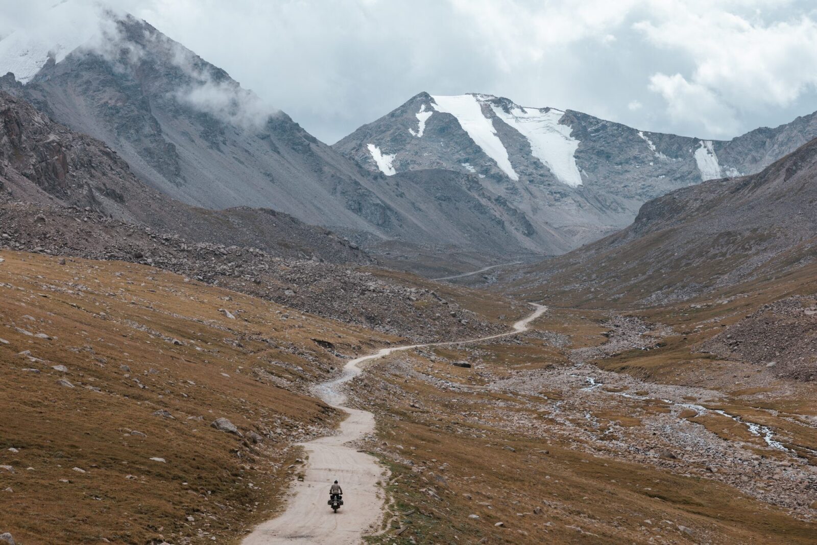 Piste de montagne vers les sommets enneigés du Tian Shan, voyage moto au Kirghizistan